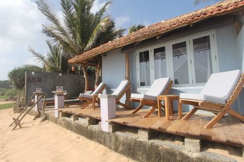 The white beachfront rooms of EKA Beach seen from the sand, with loungers on the terrace