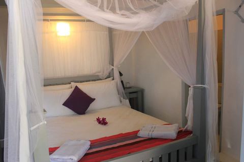 Queen bed under a white mosquito canopy in a room at EKA Beach