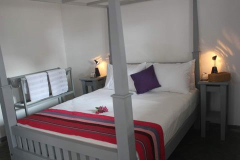 A four-poster queen bed with bedside lamps in a room at EKA Beach