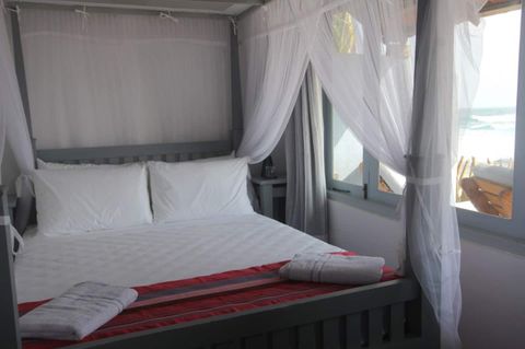 Queen bed with a mosquito net beside a window looking out to the beach
